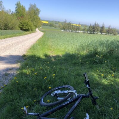 Cykel liggende på jorden mens man ser en grusvej ned langs markerne